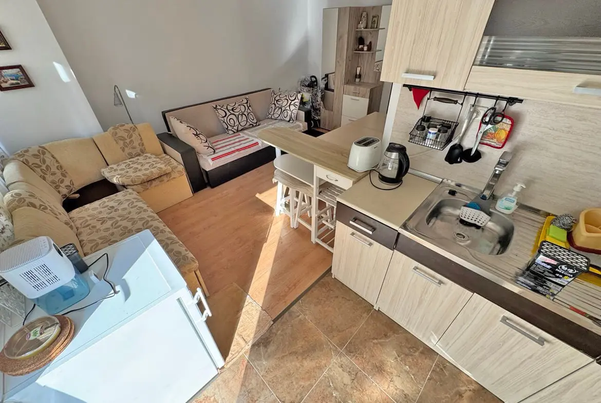 Современная квартира-студия с гостиной и кухонным уголком, светлые тона, уютная обстановка, идеально для продажи в Болгарии.