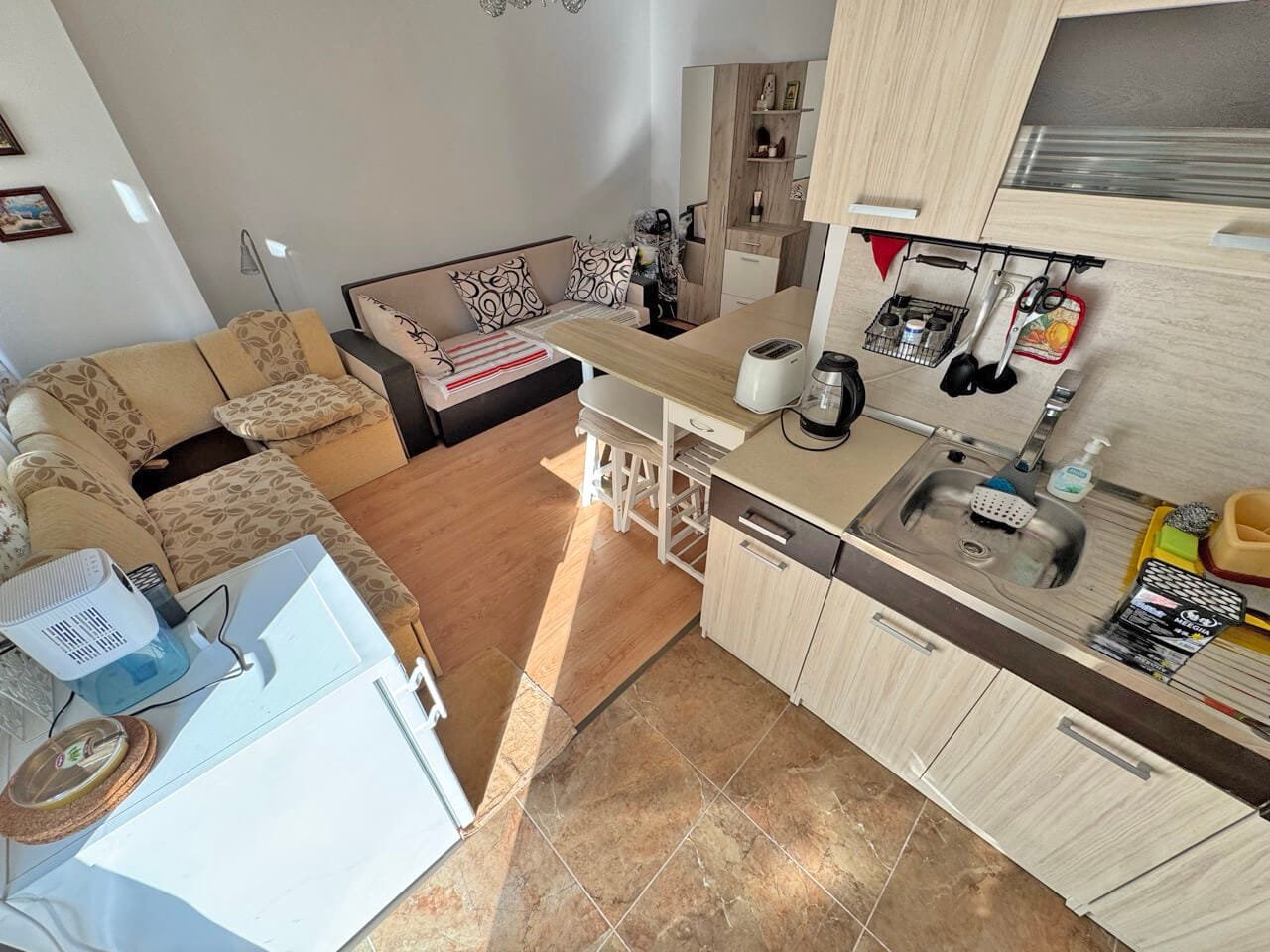 Современная квартира-студия с гостиной и кухонным уголком, светлые тона, уютная обстановка, идеально для продажи в Болгарии.