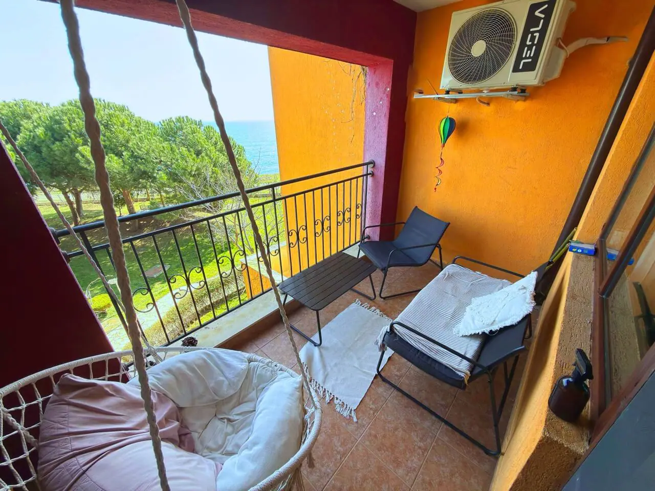 Уютная терраса с видом на море, со стильной мебелью и качелей, идеально подходит для отдыха в апартаментах.