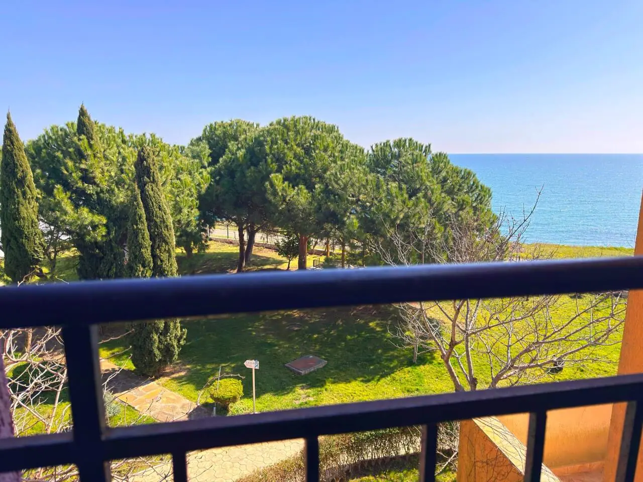 Вид с балкона на море и зелёные деревья, рядом с апартаментами у моря в Болгарии, идеальные условия для жизни.