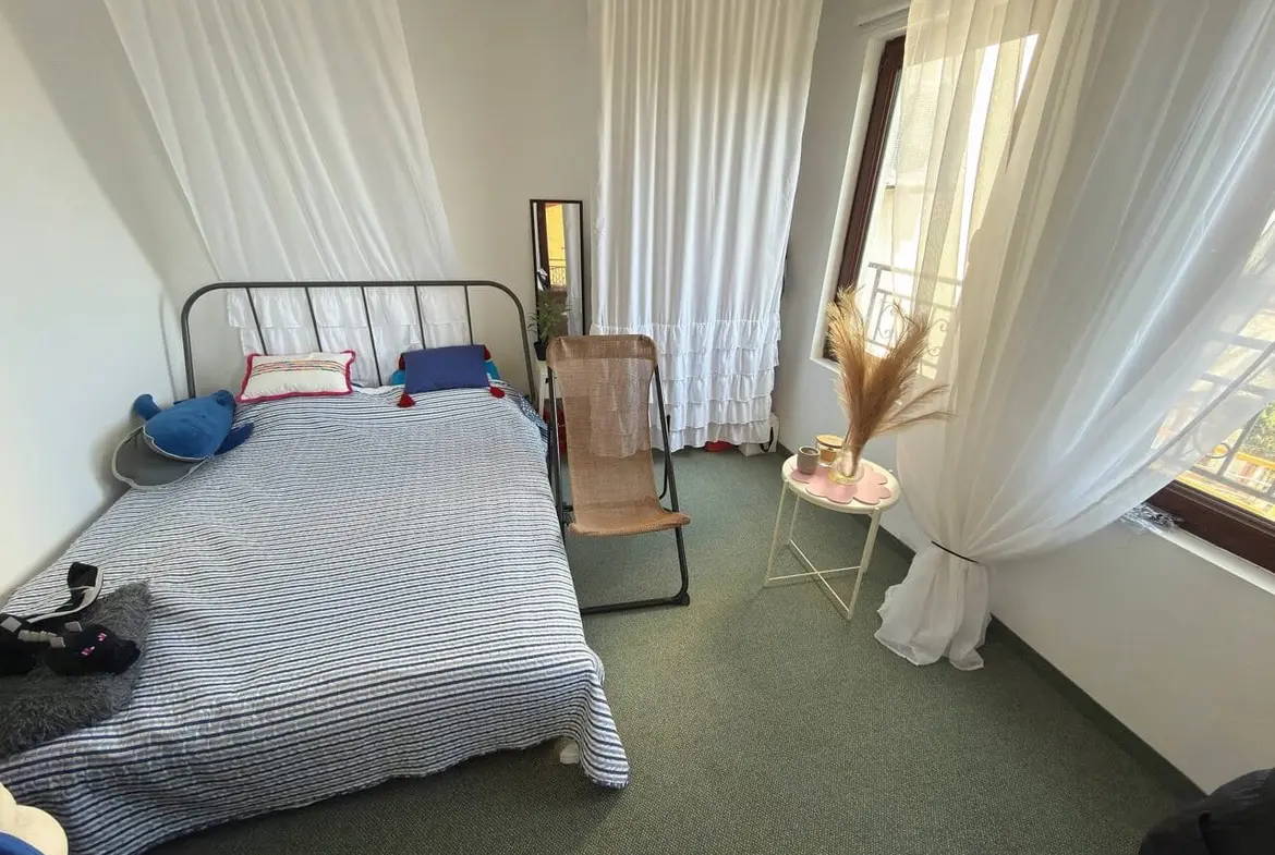 Уютная спальня с кроватью и креслом, белыми занавесками, идеальна для создания комфортного жилья в Болгарии.