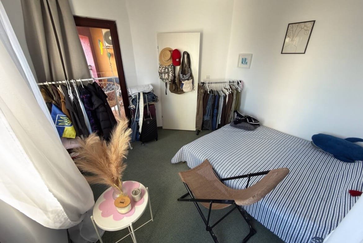 Уютная спальня с двуспальной кроватью, стилизованная в светлых тонах, с гардеробом и зоной для отдыха в квартире у моря.