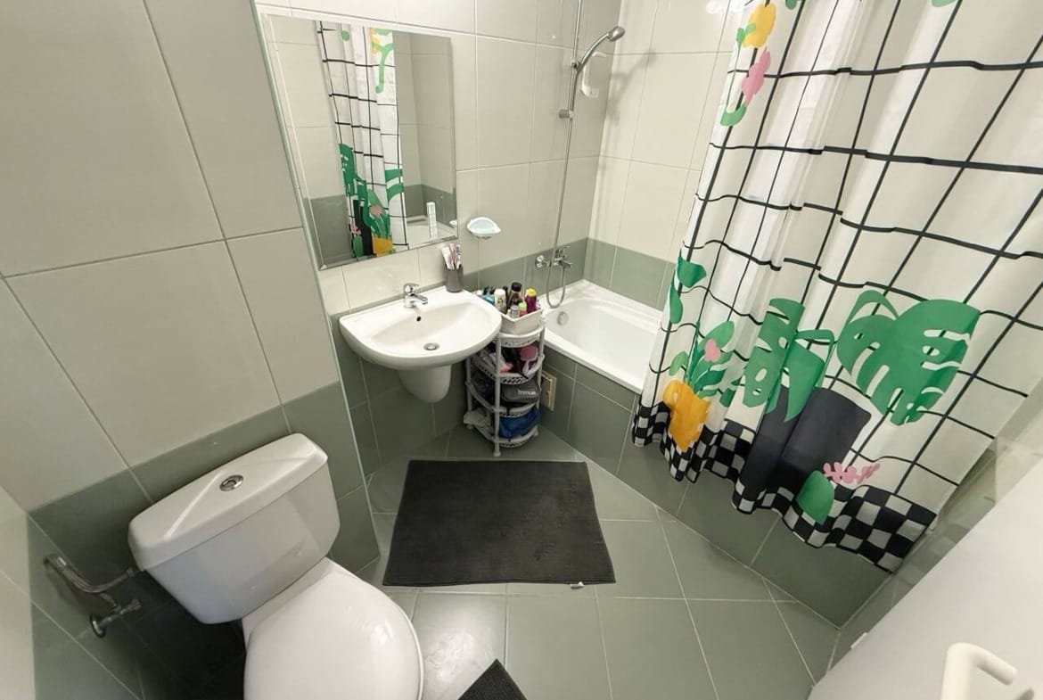 Современная ванная комната с душевой кабиной и ванной, белой сантехникой и ярким занавесом с растительным узором.