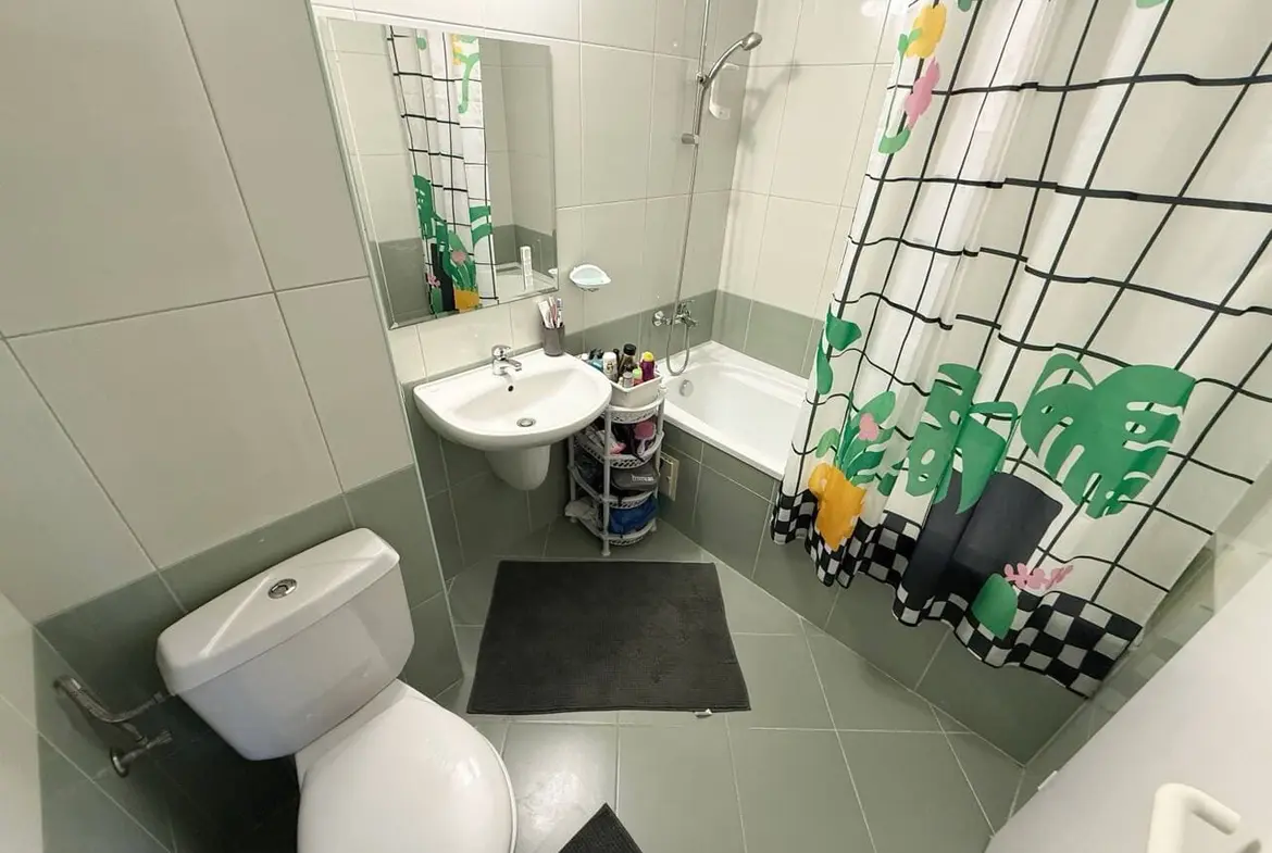 Современная ванная комната с душевой кабиной и ванной, белой сантехникой и ярким занавесом с растительным узором.