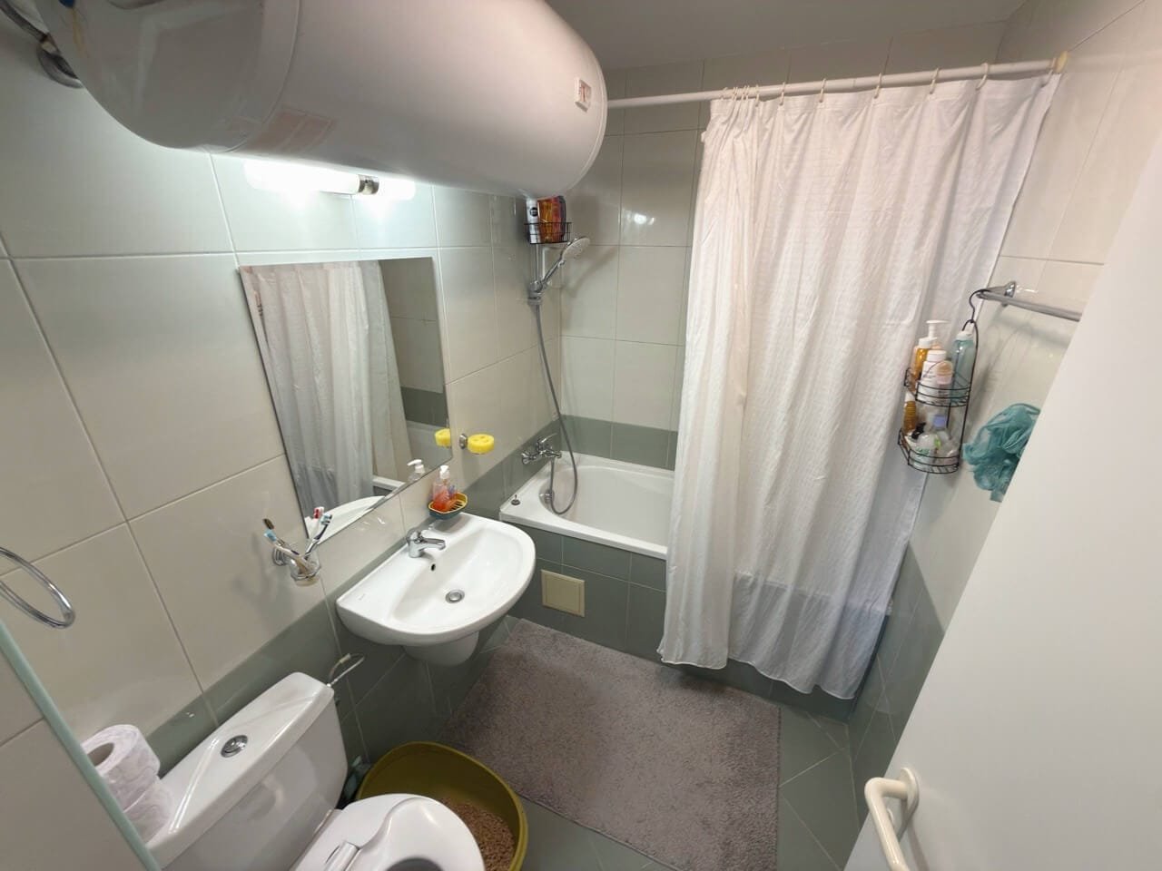 Современная ванная комната: сантехника и уютный интерьер Современная ванная комната с ванной, душевой занавеской и раковиной, акцент на чистоту и функциональность, идеальна для жилья в Бургасе.