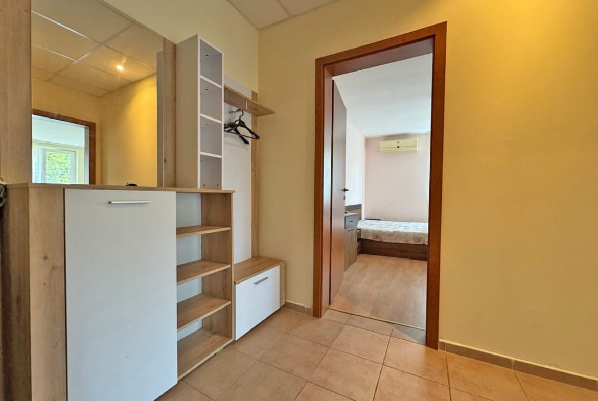 Современный интерьер коридора с шкафом, зеркалом и входом в спальню с светлыми стенами и деревянным полом.