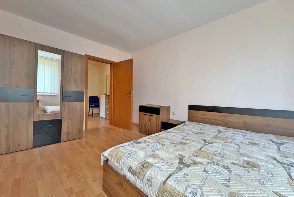 Спальня с двуспальной кроватью, деревянной мебелью, окнами с занавесками и входом в соседнюю комнату.