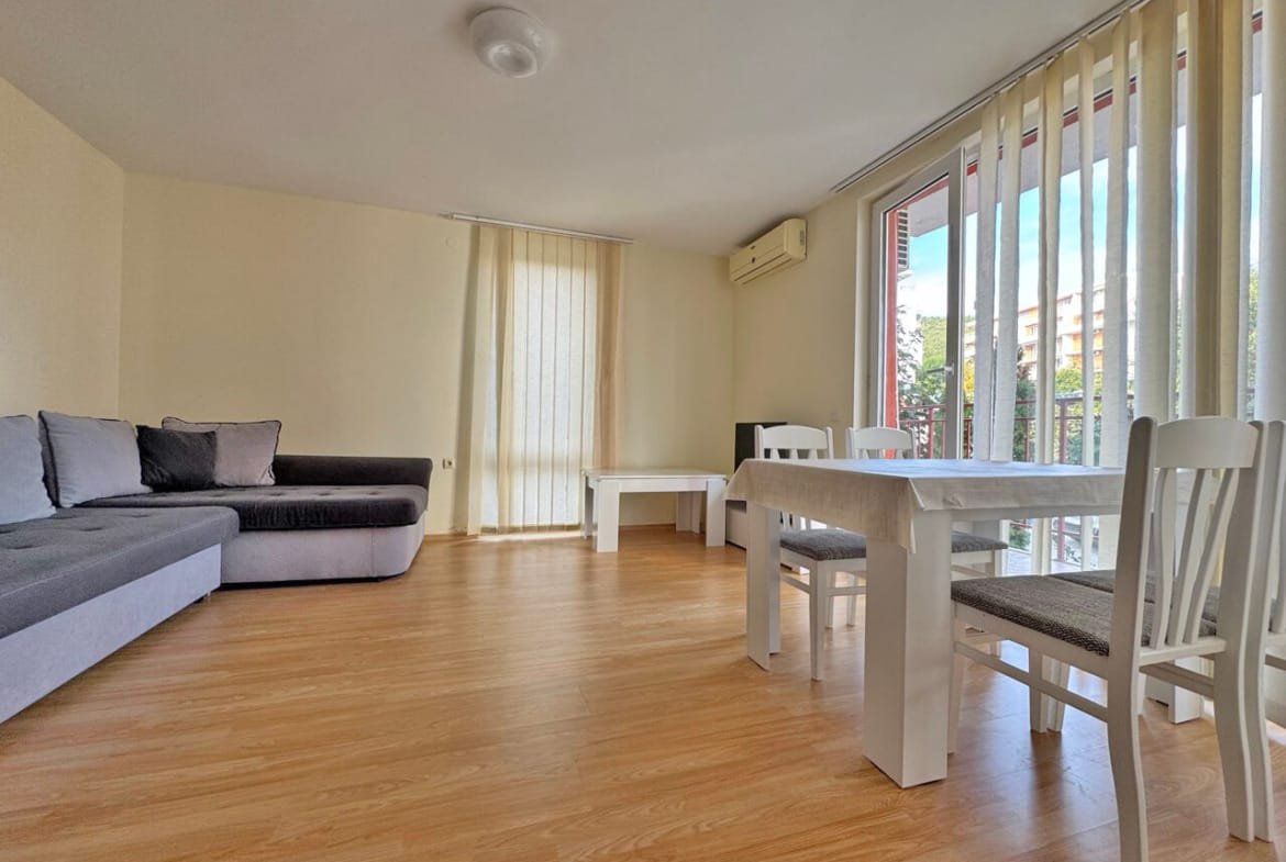 Современный интерьер квартиры с серым диваном, белыми столом и стульями, большими окнами и светлыми стенами.