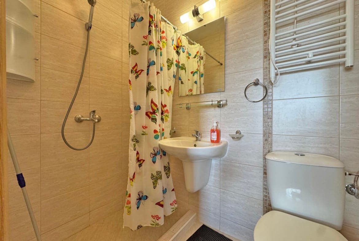 Современная ванная комната с душевой кабиной, унитазом и зеркалом, оформленная яркими тканевыми занавесками.