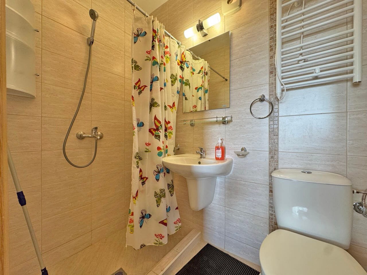 Современная ванная комната с душевой кабиной, унитазом и зеркалом, оформленная яркими тканевыми занавесками.