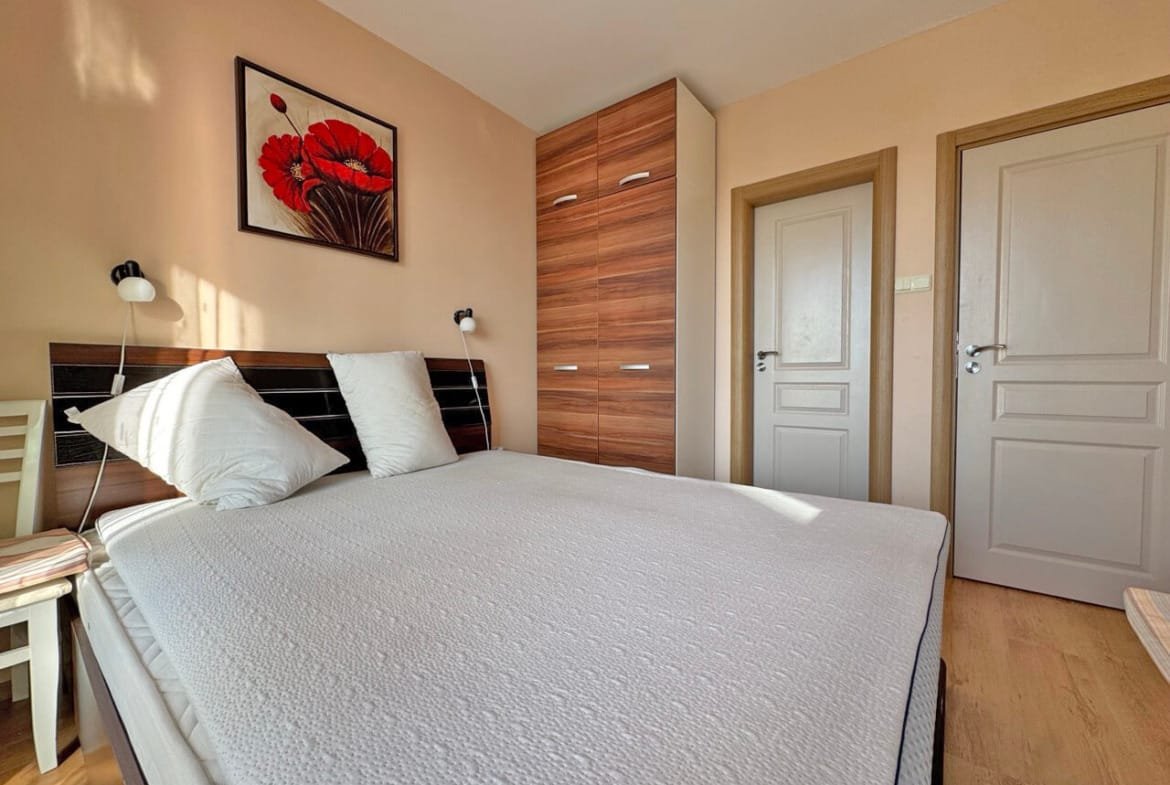 Современная спальня с большой кроватью и шкафом, яркие акценты на стене, идеальное жилье в Болгарии для отдыха или постоянного проживания.