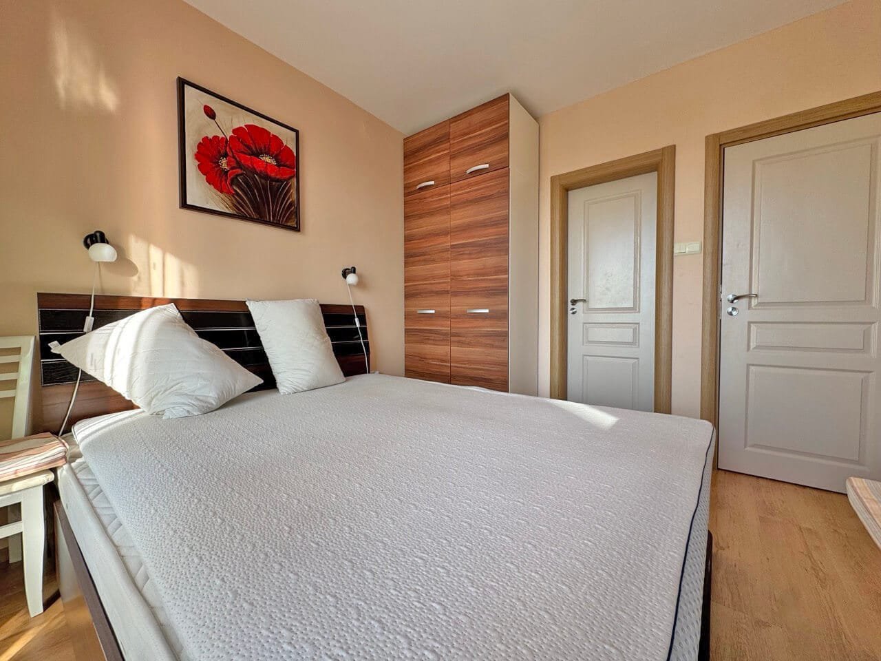 Современная спальня с большой кроватью и шкафом, яркие акценты на стене, идеальное жилье в Болгарии для отдыха или постоянного проживания.