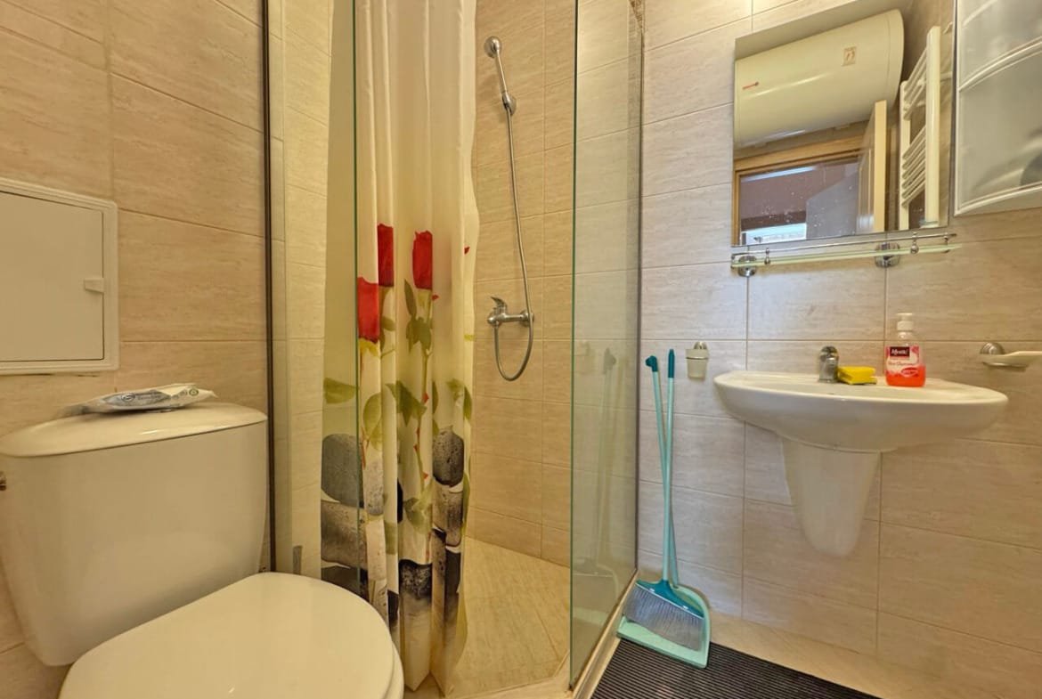 Современная ванная комната с душевой кабиной, унитазом и раковиной, оформленная в светлых тонах, идеальна для апартаментов в Болгарии.