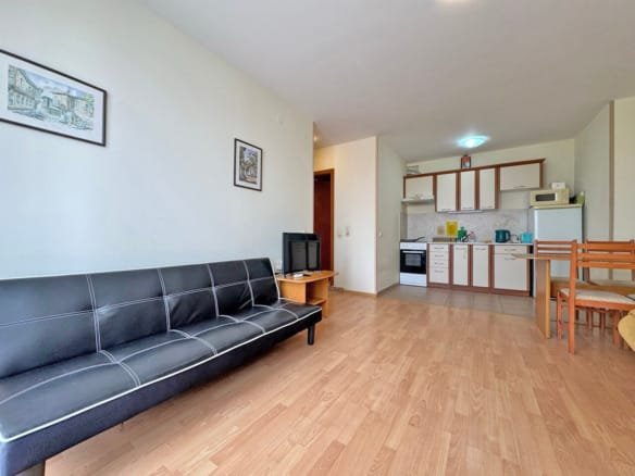 Современная гостиная с черным диваном, телевизором и кухонной зоной, оформленной в светлых тонах, пилинг деревянного пола.