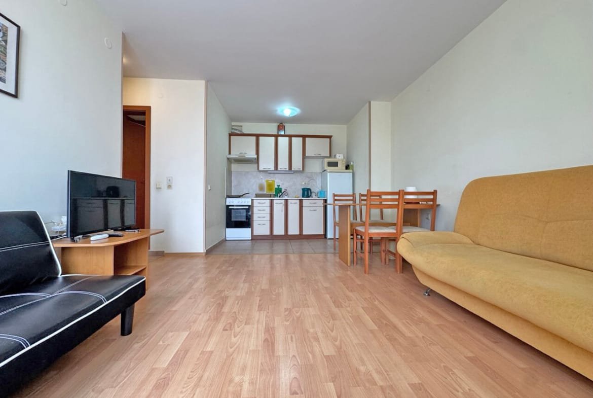 Современная квартира с открытой планировкой, кухонный уголок, обеденный стол и диван, светлые стены и деревянный пол.