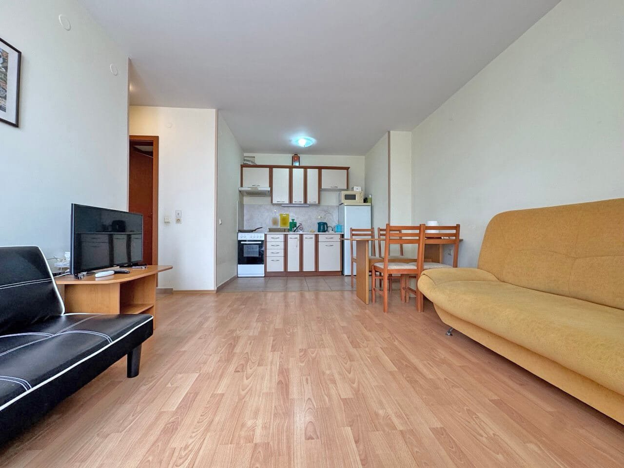 Современная квартира с открытой планировкой, кухонный уголок, обеденный стол и диван, светлые стены и деревянный пол.