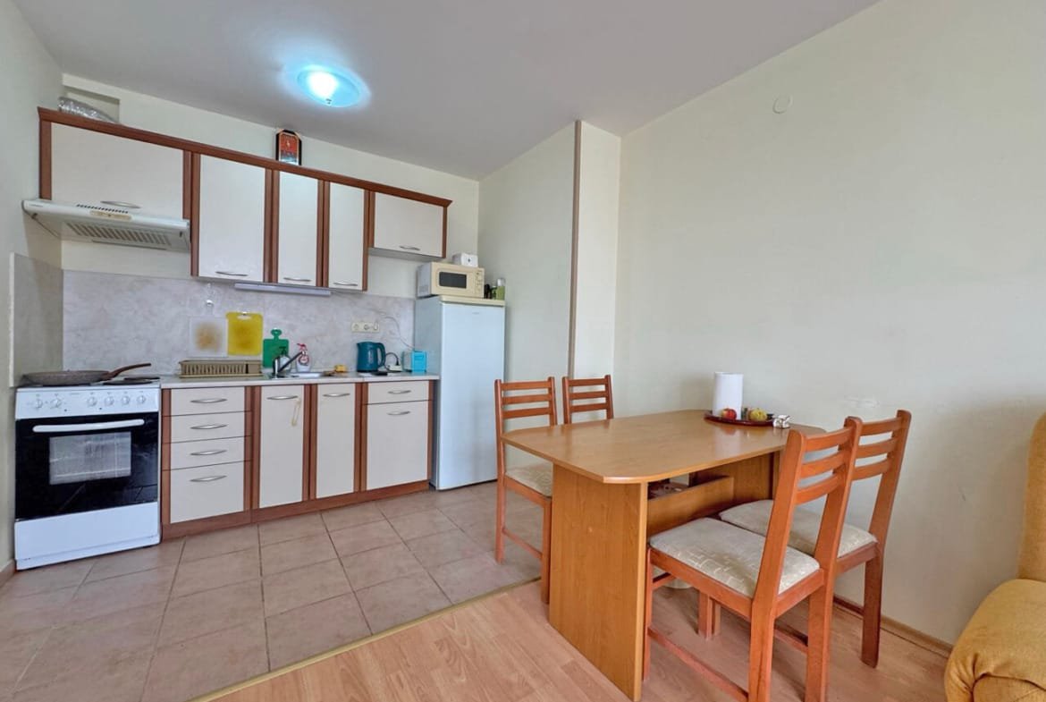 Кухня с обеденным столом, стульями, плитой, холодильником и микроволновой печью, светлые стены и пол.