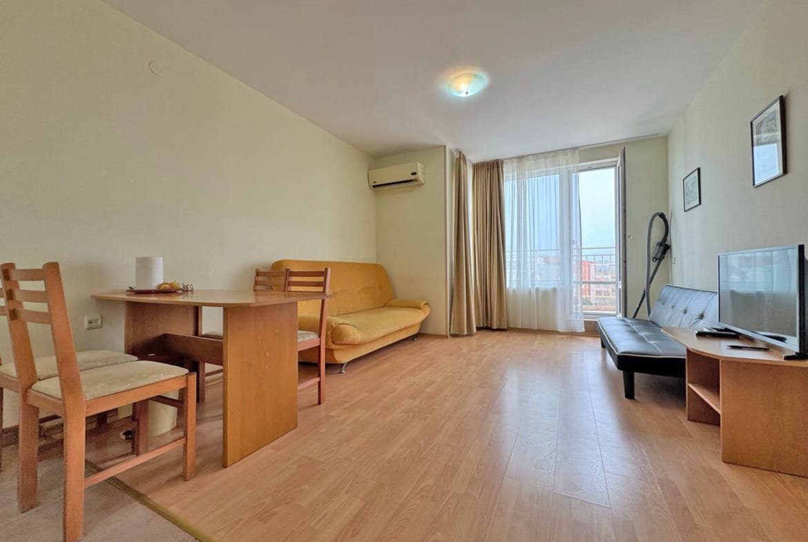 Светлая квартира с диваном, столом и стульями, большим окном и телевизором, оформленная в нейтральных тонах.