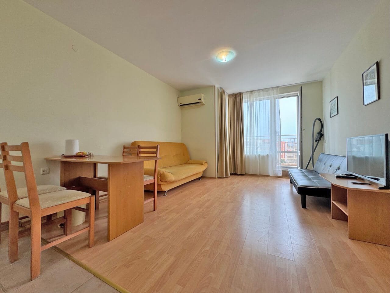 Светлая квартира с диваном, столом и стульями, большим окном и телевизором, оформленная в нейтральных тонах.