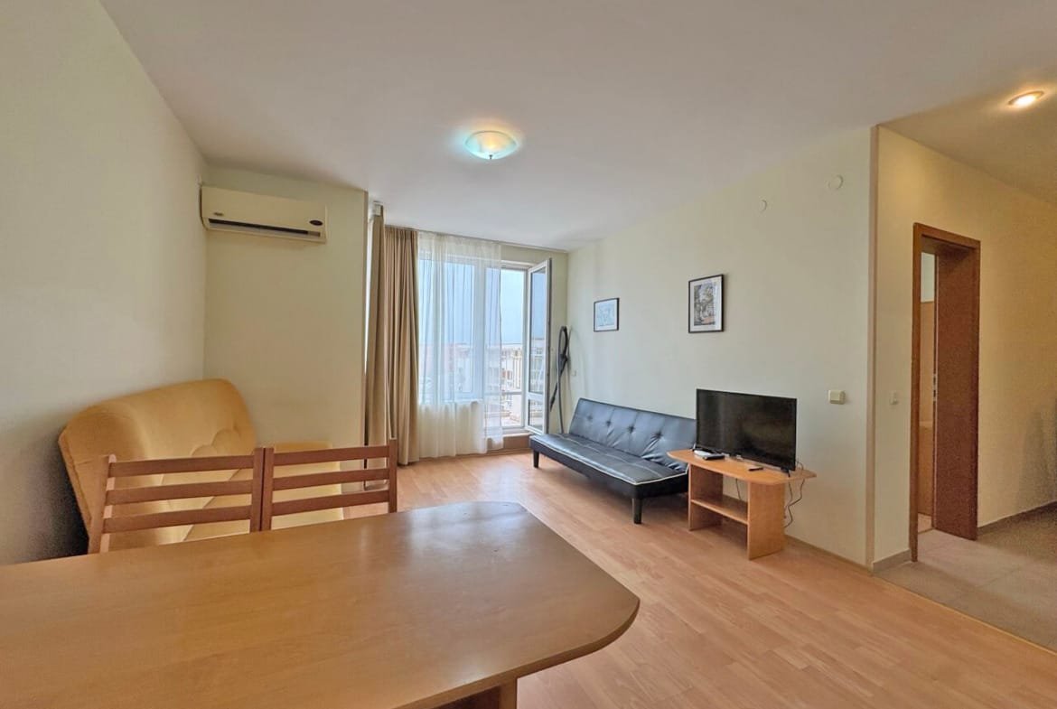 Гостиная с диваном, креслом и телевизором, большой панорамный窗, светлые стены и деревянный пол.