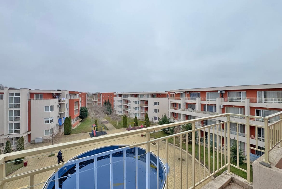 Жилой комплекс с несколькими зданиями, внутренним двором и бассейном, серое небо на фоне.