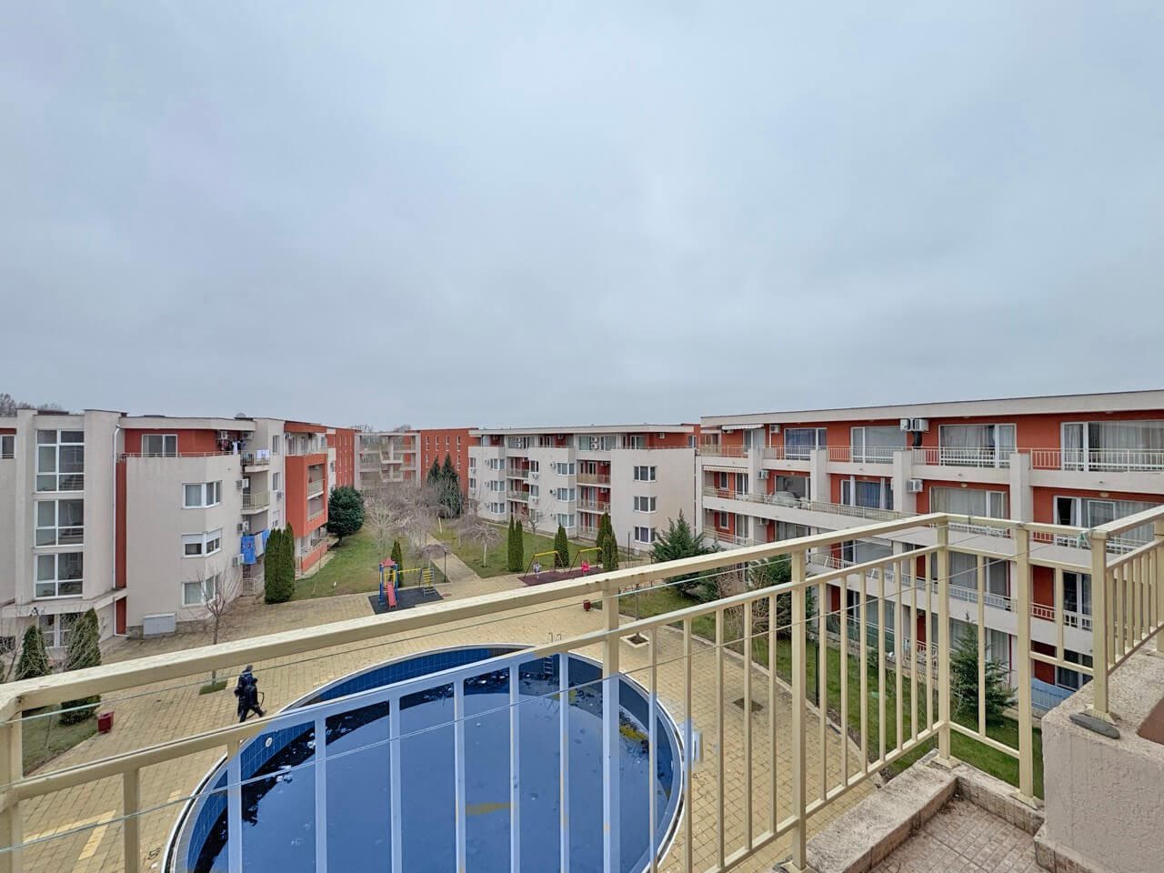 Жилой комплекс с несколькими зданиями, внутренним двором и бассейном, серое небо на фоне.