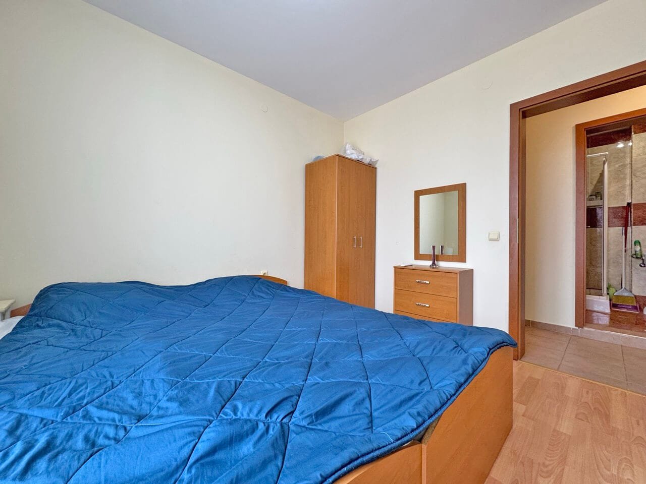 Спальня с двуспальной кроватью, шкафом, комодом и ванной в углу. Преобладают светлые оттенки синих и коричневых цветов.