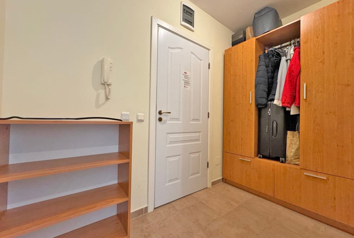 Уютный прихожая с деревянным шкафом для одежды, полками и белой дверью, оформленная в светлых тонах.