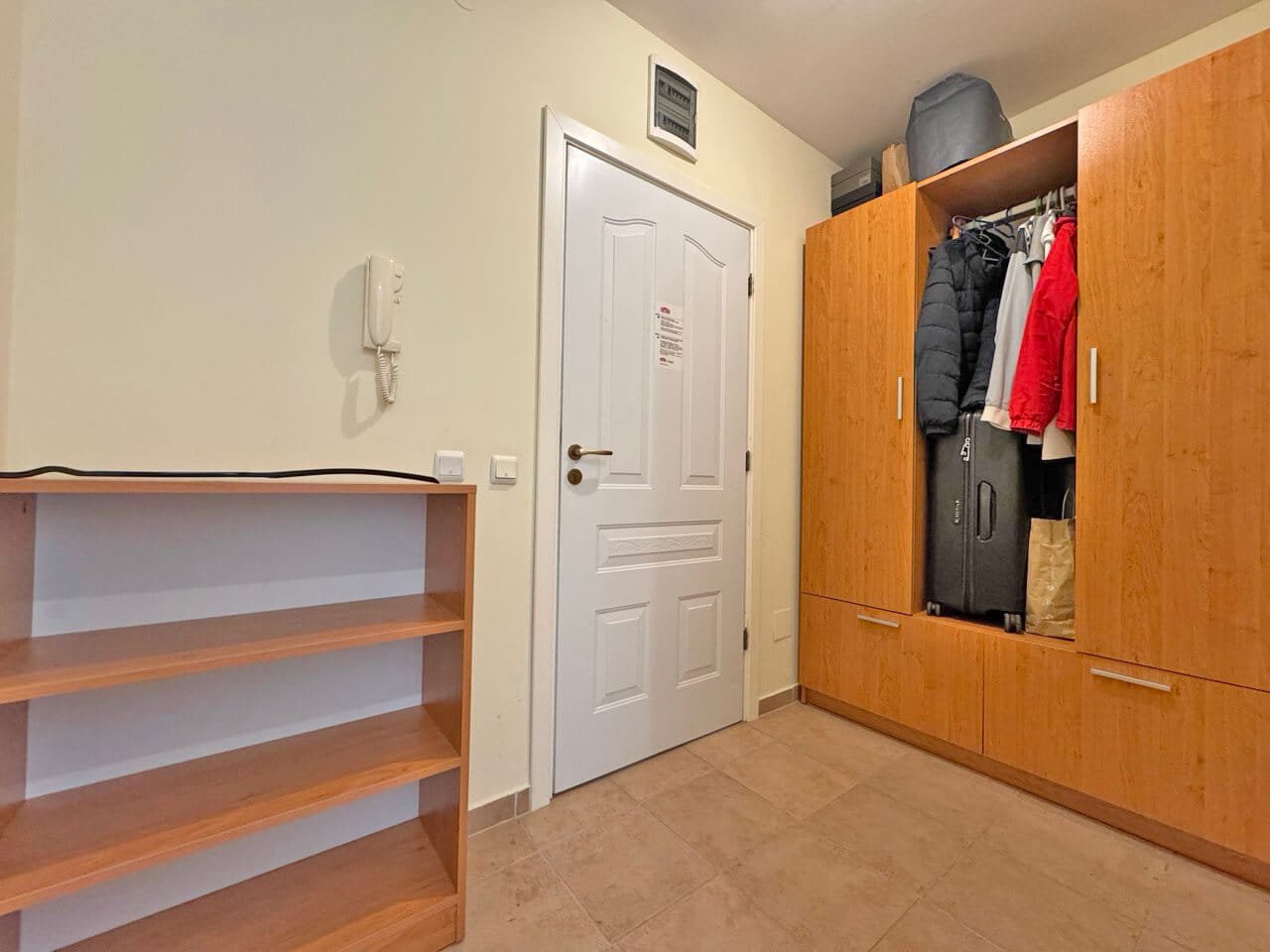 Уютный прихожая с деревянным шкафом для одежды, полками и белой дверью, оформленная в светлых тонах.