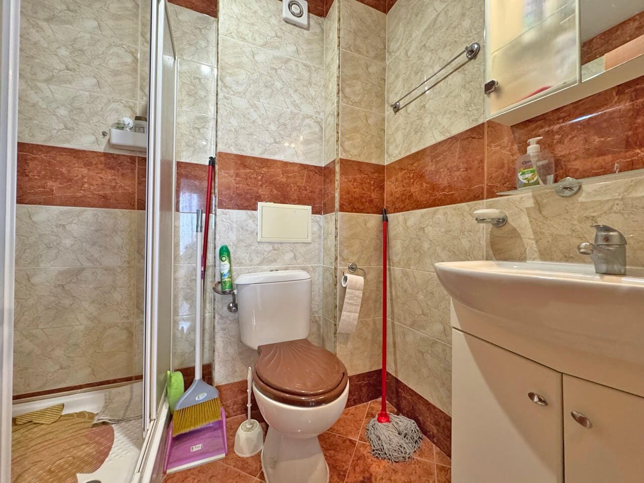 Современная ванная комната с душевой кабиной, унитазом и раковиной, стены отделаны плиткой в светлых и коричневых оттенках.