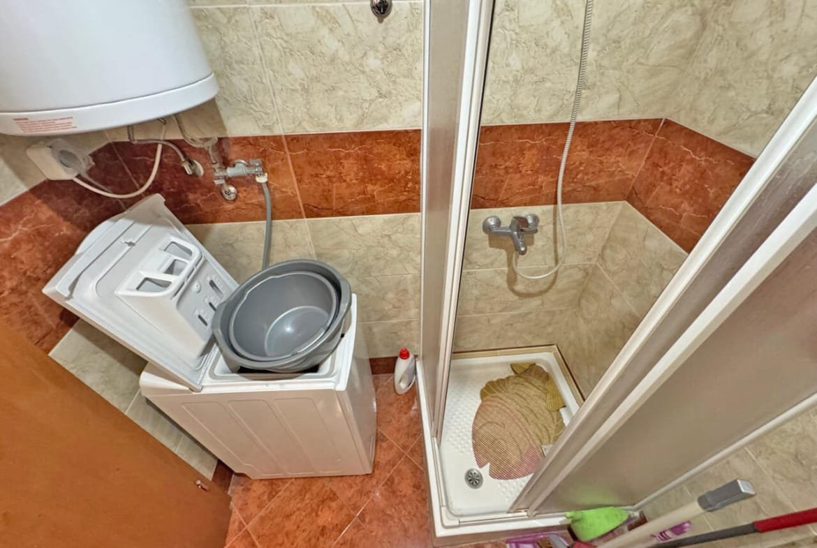 Стиральная машина рядом с душевой кабиной и раковиной в ванной комнате с мраморными стенами и плиткой.