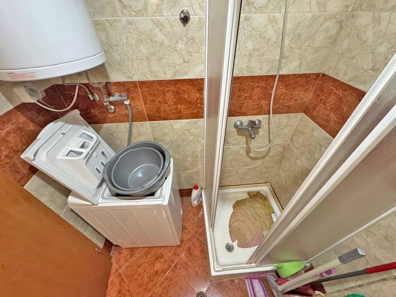 Стиральная машина рядом с душевой кабиной и раковиной в ванной комнате с мраморными стенами и плиткой.