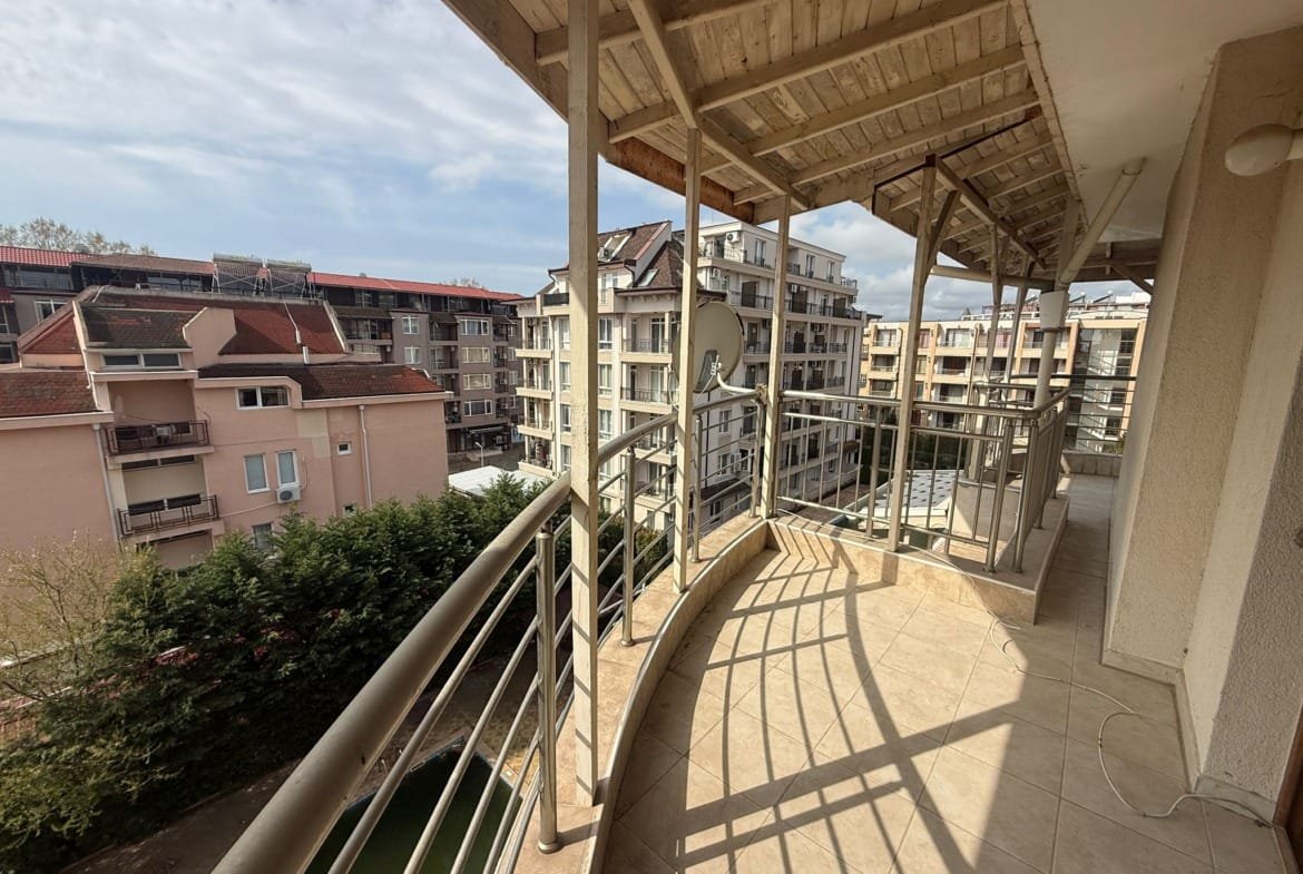 Балкон квартиры в Болгарии с видом на жилые здания и зелень, идеальное место для отдыха и наслаждения природой.