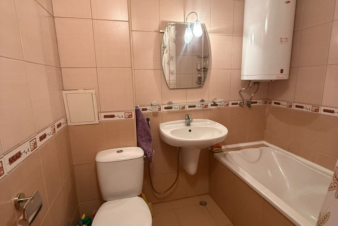 Современная ванная комната с ванной, раковиной и унитазом, оформленная в светлых тонах, подходящая для покупки жилья в Болгарии.