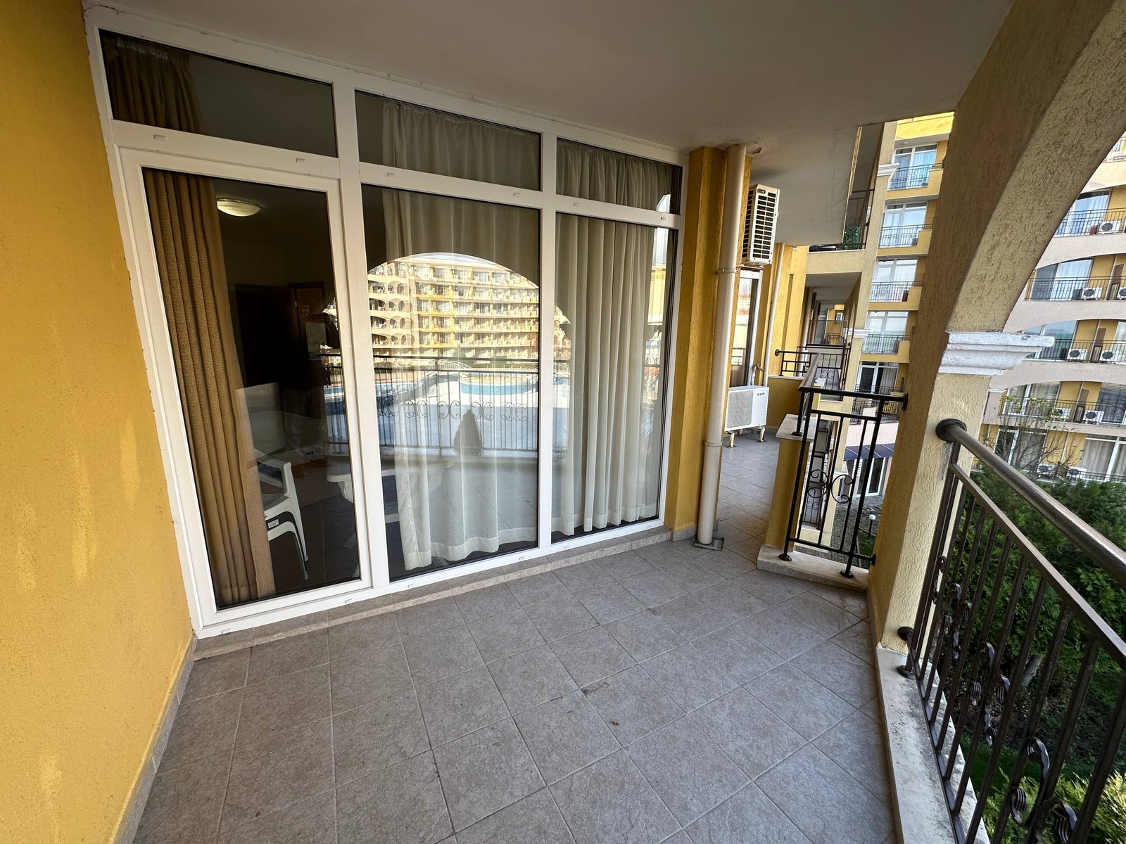 photo_10_2025-12-09_19-05-49 Балкон с плиточным покрытием и стеклянными дверями, вид на соседние здания и зеленую территорию.