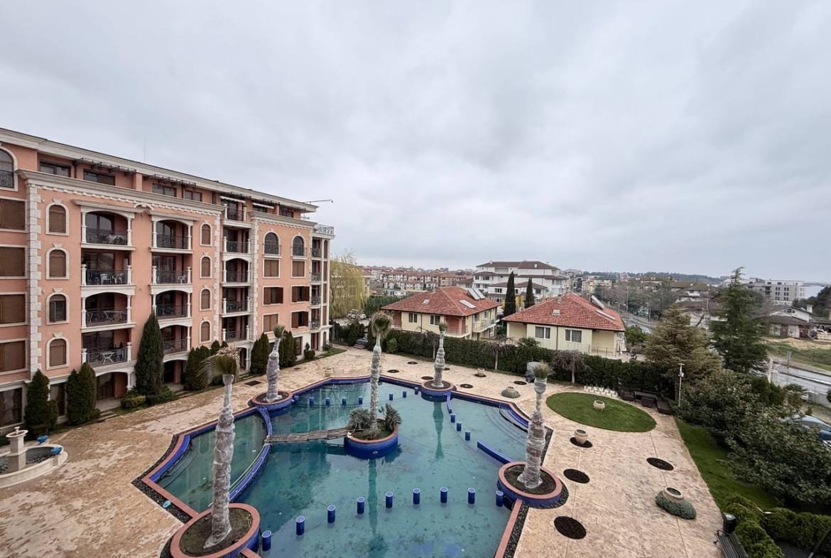 Жилая недвижимость в Болгарии с бассейном и фонтанами на фоне облачного неба и окружающих вилл.