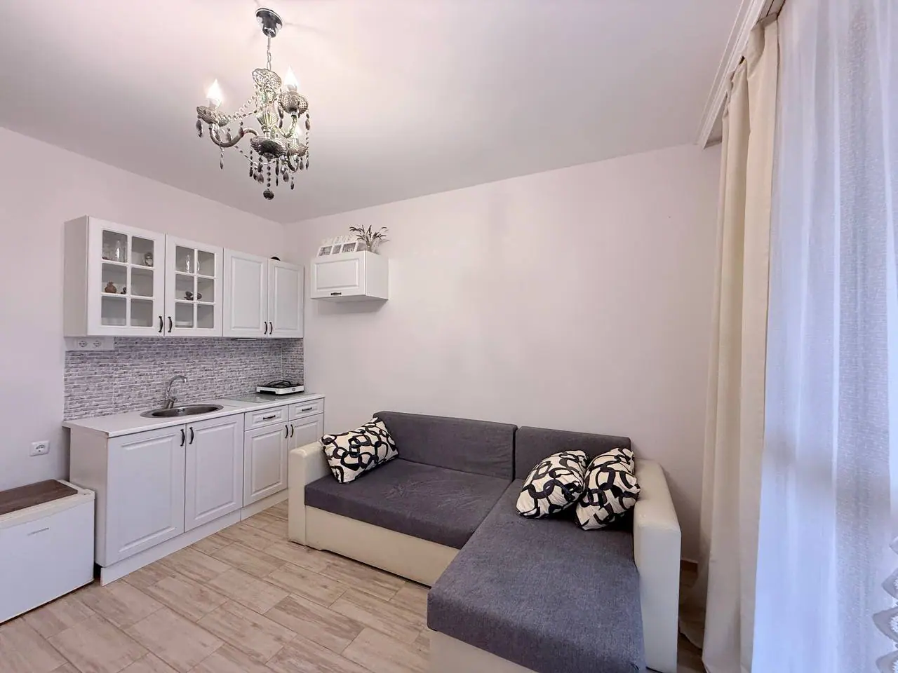 Современный интерьер небольшой кухни-гостиной с диваном. Современная квартира со светлым интерьером, уютным диваном и кухонным гарнитуром, идеально подходящая для продажи в Болгарии.