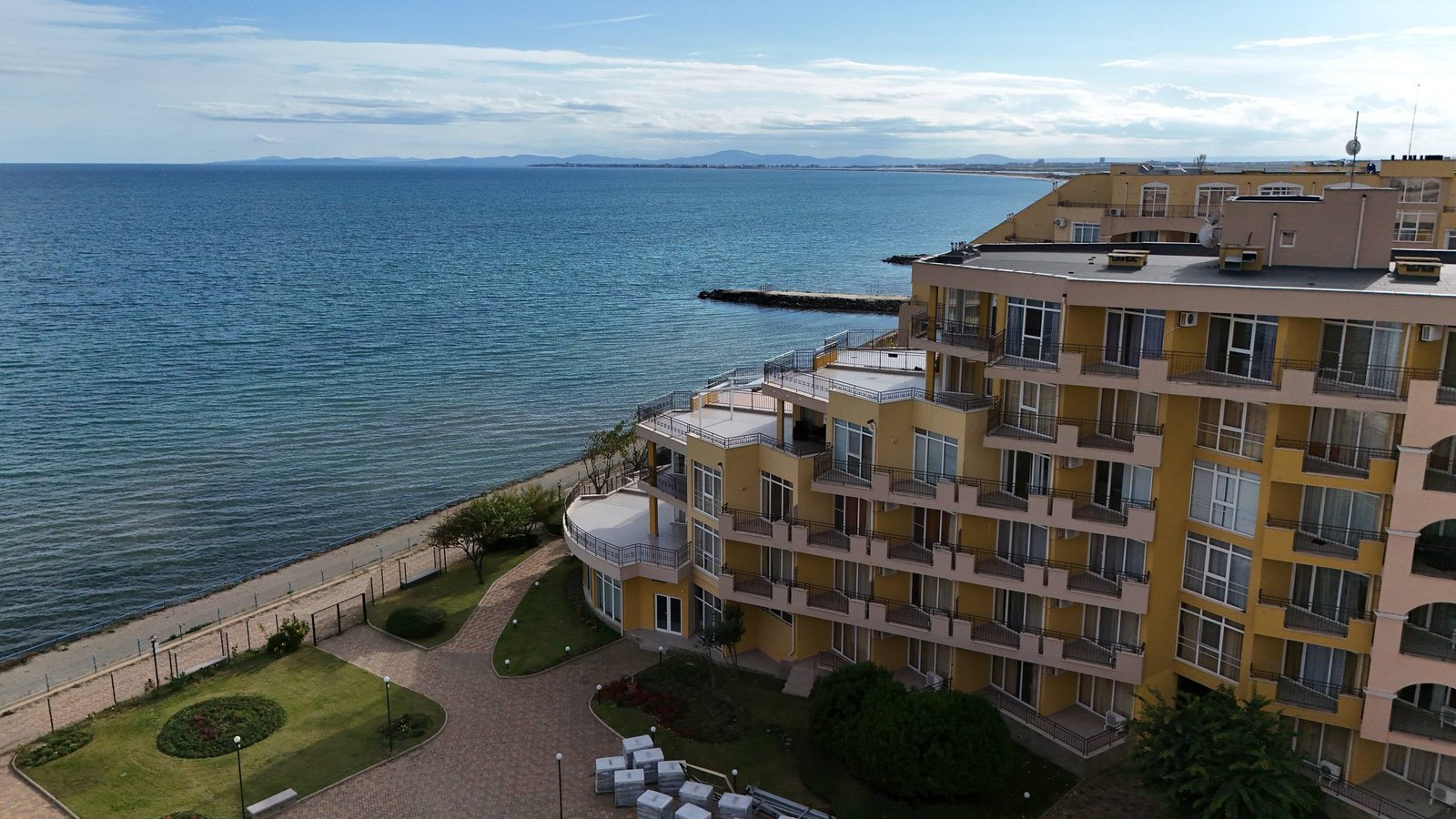 photo_1_2025-12-09_19-10-27 Современный жилой комплекс у моря с зелеными насаждениями и пешеходной дорожкой вдоль пляжа.