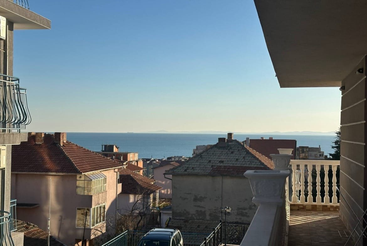 Вид на море и жилые дома из двухкомнатного апартамента в Roel Residence, ясный день, голубое небо.