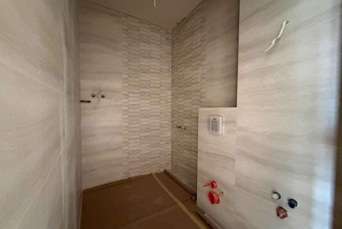 Современный интерьер ванной комнаты в студии, отделка светлыми плитками и установленная сантехника.