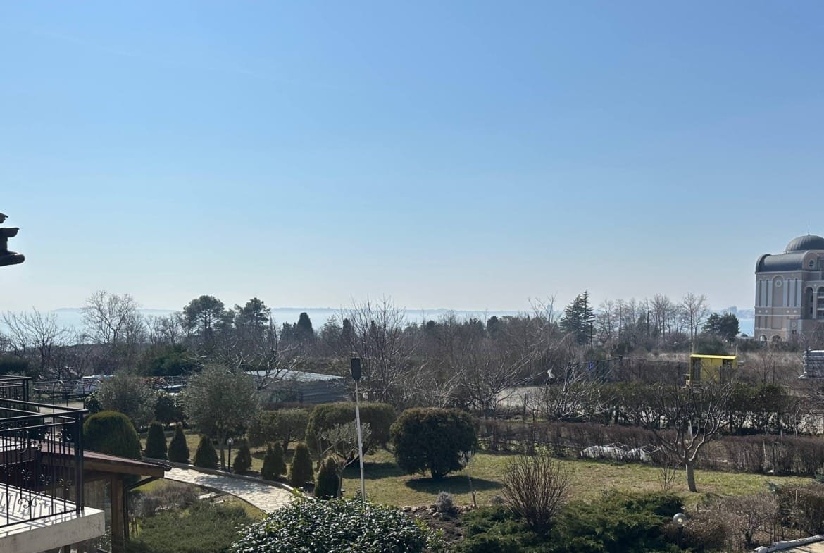 Вид с балкона на зеленый ландшафт, вершины деревьев и море под ясным небом. Создает атмосферу спокойствия и комфорта.