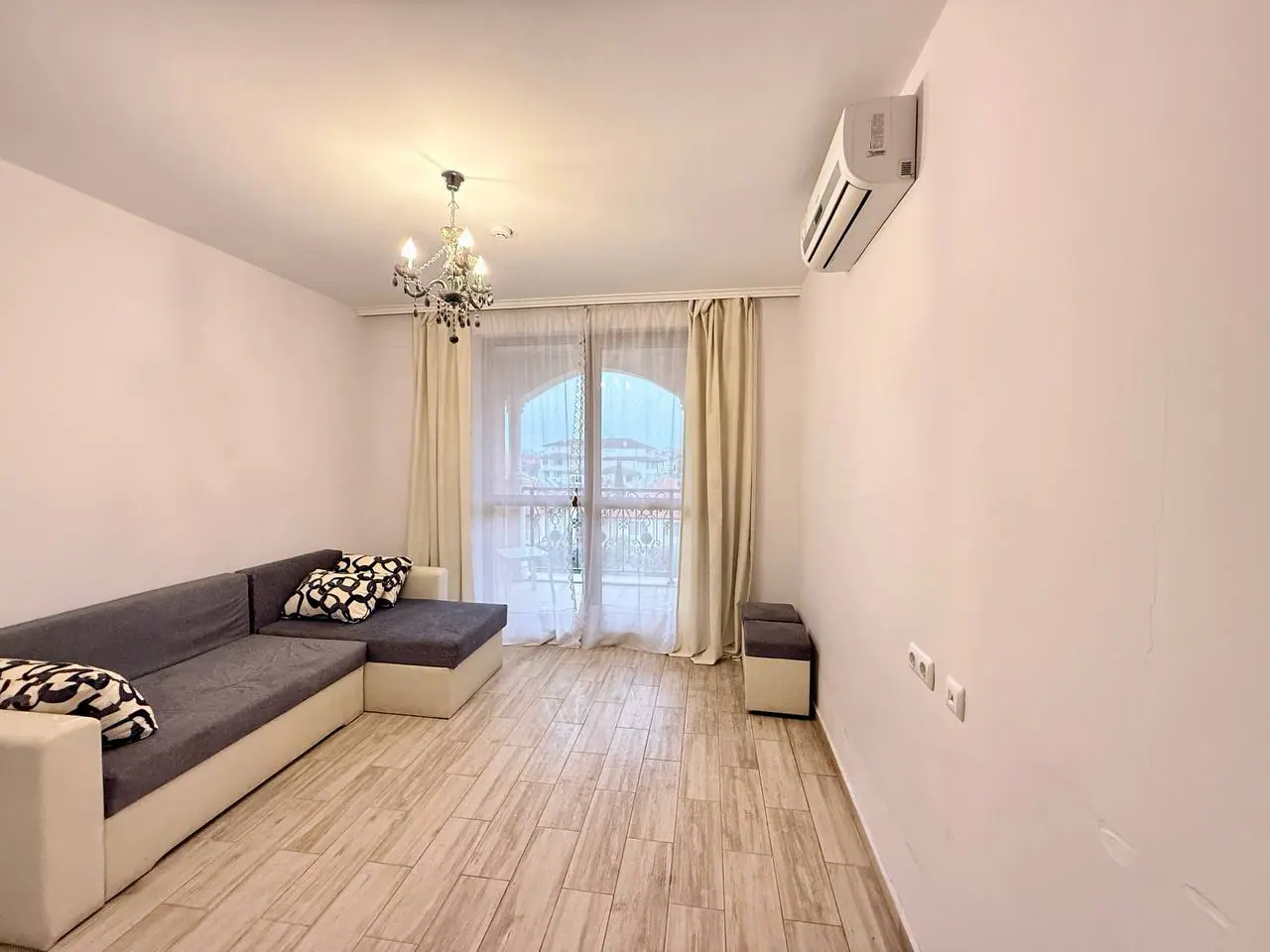 Современный интерьер квартиры с светлым дизайном и балконом Светлое помещение с диваном, с балконной дверью и современным дизайном, идеально для покупки недвижимости в Болгарии.