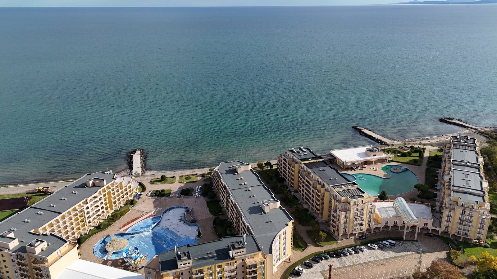 photo_2_2025-12-09_19-05-49 Красивая панорама курортного комплекса с бассейнами и пляжем у моря, спокойная вода и зеленые насаждения.
