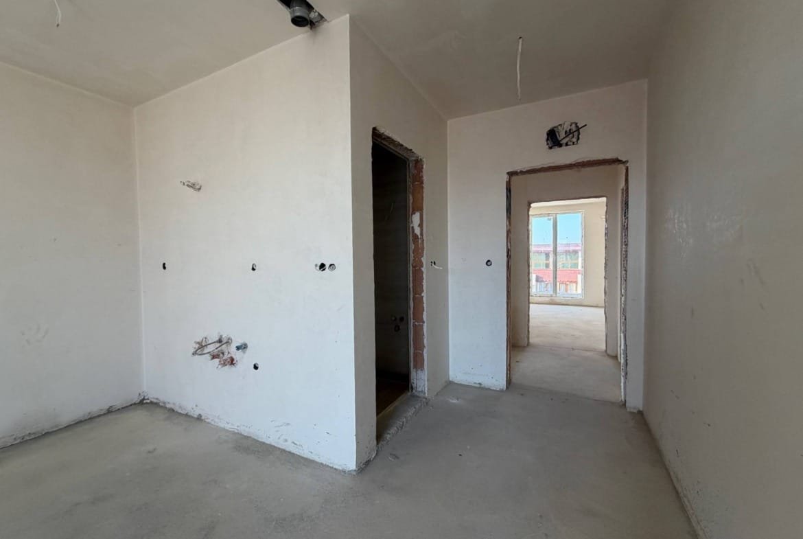 Пустая студия с оштукатуренными стенами, дверными проемами и незавершенной отделкой, окно с видом на улицу.