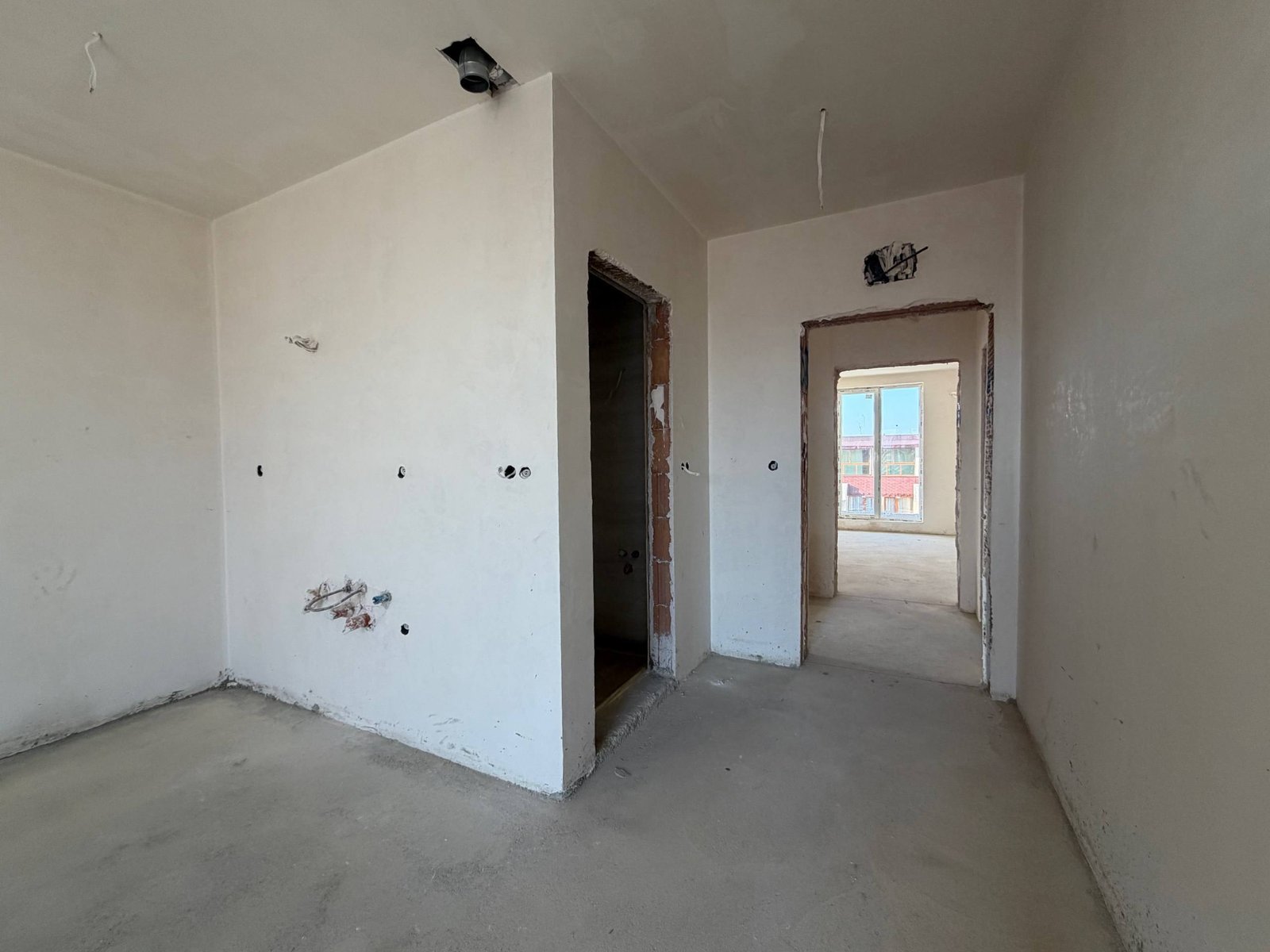 Пустая студия с оштукатуренными стенами, дверными проемами и незавершенной отделкой, окно с видом на улицу.