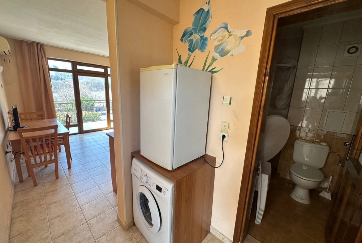 Двухкомнатный апартамент с белым холодильником, стиральной машиной и ванной, которые создают комфортную атмосферу.