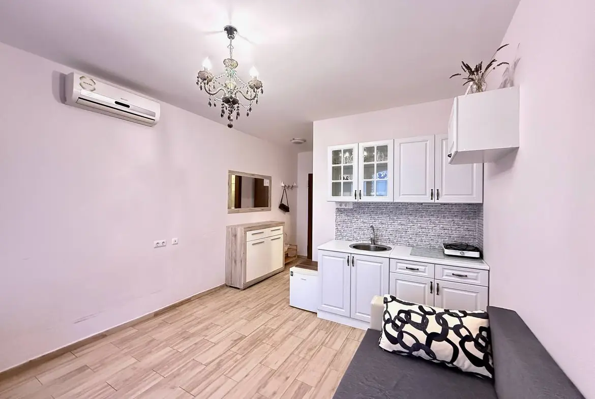 Современная квартира в Болгарии с кухонным уголком, светлыми стенами и деревянным полом, идеальная для покупки или аренды.