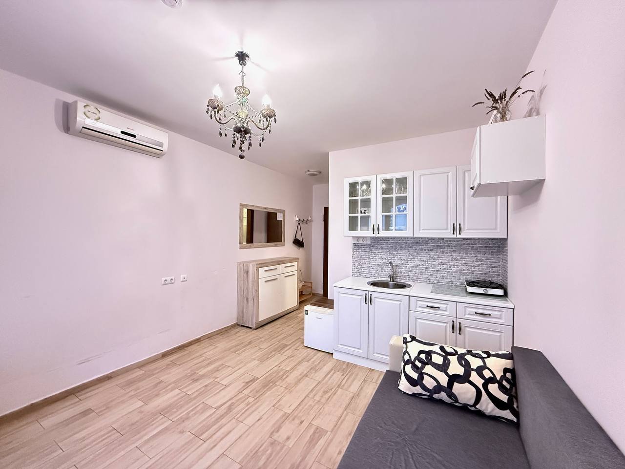 Современная кухня-студия с уборной и светлым интерьером Современная квартира в Болгарии с кухонным уголком, светлыми стенами и деревянным полом, идеальная для покупки или аренды.