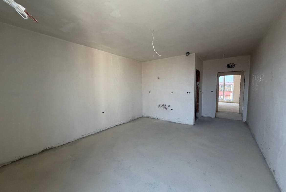 Пустая студия в комплексе La Mer Gold с белыми стенами, бетонным полом и естественным освещением, готовая к отделке.