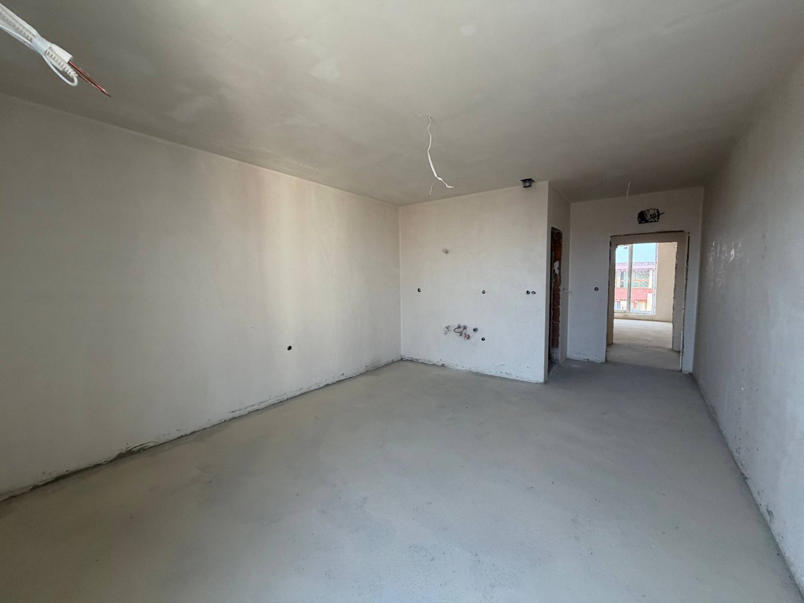 Пустая студия в комплексе La Mer Gold с белыми стенами, бетонным полом и естественным освещением, готовая к отделке.